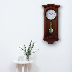 a clock on the wall next to a table with a plant in it and an elephant figurine