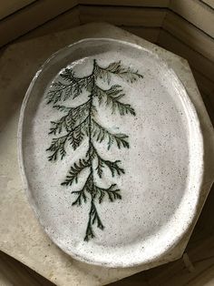 a white plate with green designs on it sitting on top of a wooden table next to a window