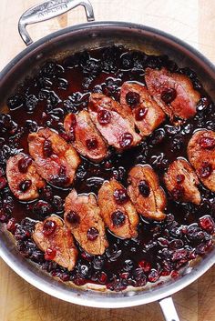 meat and berries cooking in a pan on a wooden counter top with utensils