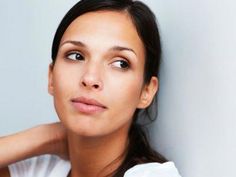 a woman with her hand on her shoulder looking at the camera while leaning against a wall