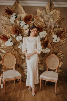 a woman standing next to two chairs in front of a wall with flowers