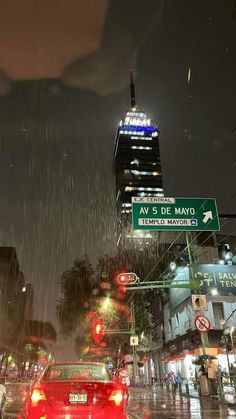 cars are driving down the street in the rain at night with buildings and traffic lights behind them