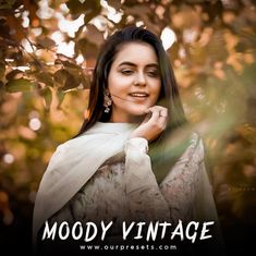 a woman with long black hair wearing a white shawl and posing in front of trees