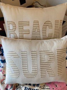 two pillows that are sitting on top of a bed with the words beach surf printed on them