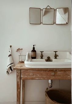 a white sink sitting under three mirrors in a bathroom next to a wooden table with two soap dispensers on it