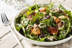 a salad with bacon, onions and lettuce in a white bowl on a table