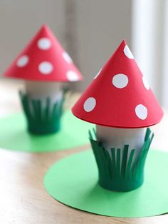 two red and white mushrooms sitting on top of green paper cups with grass growing out of them