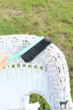 a person holding a brush on top of a wicker chair in the grass,