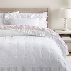 a white bed with pink ruffles and pillows