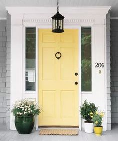 a yellow front door with two potted plants next to it and a light hanging from the ceiling