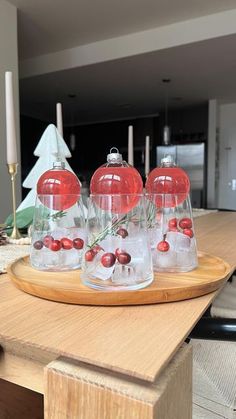 four clear glass vases with red berries and greenery in them on a wooden tray