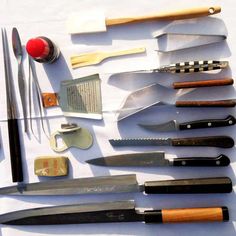 many different types of knives are laid out on a white tablecloth with red and black trimmings