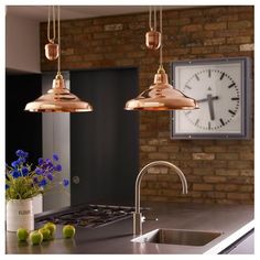 two lights hanging over a kitchen counter next to a sink and clock on the wall