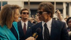 a man and woman talking to each other in front of a group of people holding microphones