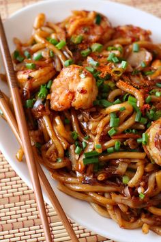 a plate full of noodles with shrimp and chopsticks