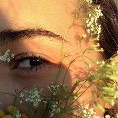 a woman's eyes and flowers in front of her face, with the sun shining through