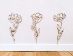 three metal flowers on a wooden floor next to a white wall