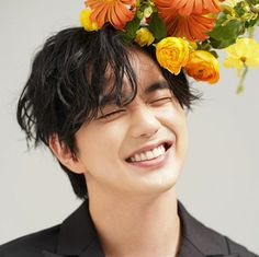 a man with flowers on his head smiling at the camera while wearing a blazer