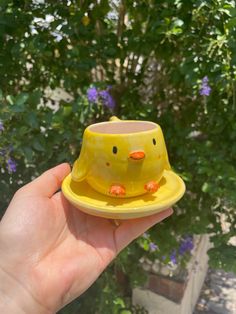 a hand holding a small yellow cup with orange birds on it's top and bottom