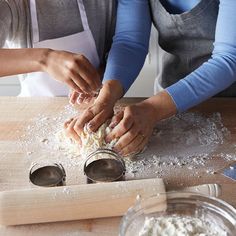 two women in aprons are preparing food on a wooden table