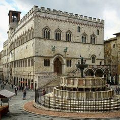 an old stone building with a fountain in front of it and people walking around the courtyard