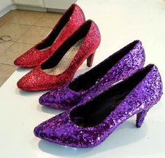 three pairs of purple and red glitter high heeled shoes on a counter in a kitchen