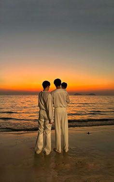 three men standing on top of a beach next to the ocean at sundown in front of an orange and blue sky