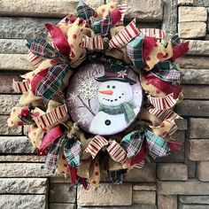 a snowman wreath on the side of a brick wall with red and green bows