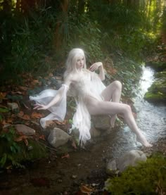 a woman with white hair is sitting on rocks in the water and posing for a photo