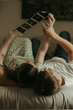 a woman laying on top of a bed holding an electronic device above her head with both hands