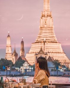 a woman sitting at a table in front of a building with spires on it