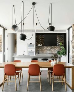 a dining room table and chairs in front of an open kitchen area with brick walls