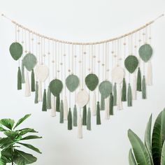 a wall hanging with green and white tassels next to a potted plant