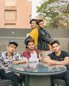 four young men sitting at a table with their arms around each other