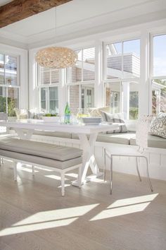 the sun shines through the large windows in this white dining room with bench and window seat