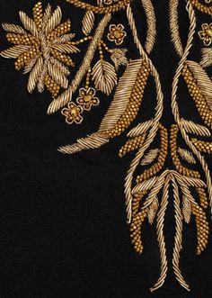 an embroidered design on black fabric with gold flowers and leaves in the center, as well as other decorative details