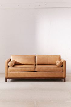 a tan leather couch sitting on top of a hard wood floor next to a white wall