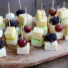 small appetizers are arranged on a wooden platter with grapes, cheese and blackberries