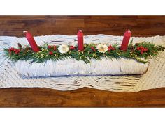 three candles are sitting on top of a white piece of cloth with greenery and flowers