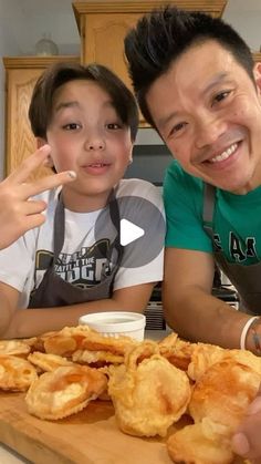 two people sitting at a table with food in front of them and one person pointing to the camera