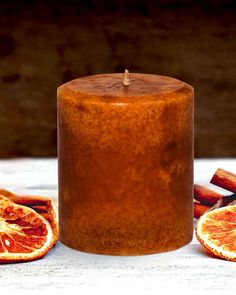 a candle with cinnamon sticks and blood oranges next to it