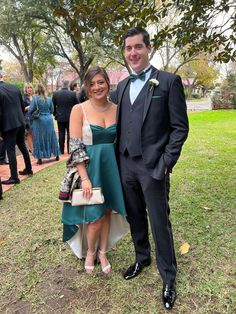 two people standing next to each other in front of some trees and grass at a formal event