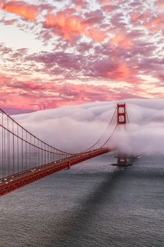 the golden gate bridge in san francisco, california is shrouded with clouds as the sun sets