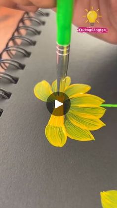 someone is drawing a sunflower on a notebook with a green marker and pen in front of it