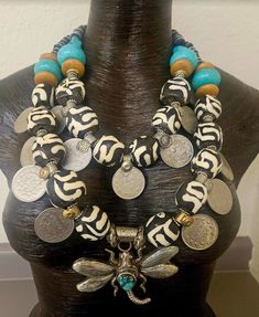 Hello Gorgeous! This big, bold and chunky Zebu* batik bone and Kuchi coin Statement Necklace is for jewelry addicts only! This OOAK piece contains the following components: bone, silver tone metal spacers, vintage Kuchi coins, turquoise-green colored Magnesite rondelles, juniper wood rondelles, Yoruba brass rings, aluminum-wood beads and faceted crystals. This is versatile in that you can flatten the coins on the interior strand or layer them on top of the outer strand (see photographs). Adjusts from 23-26". The Tibetan Repousse Dragonfly Pendant measures 3.25" x 3.5" and features an inlaid turquoise cabochon. Closes with a silver tone lobster claw clasp and a 3" extender chain with Kuchi coin dangle. Totally Haute Couture! *The bone used in this piece is from African domesticated cattle k Luxury Large Bead Amulet Jewelry, Rocker Chic Accessories, Thrift Boutique, African Jungle, Juniper Wood, Artisan Jewelry Necklaces, Brass Rings, Unique Pendant Necklace, Tibetan Jewelry