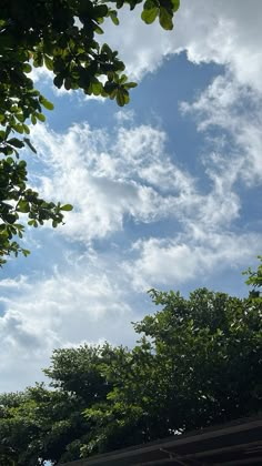 the sky is filled with clouds and green trees are in the foreground, as seen from below