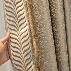 a person is holding up a curtain with a leaf pattern on it