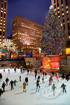 many people skating on an ice rink in front of a christmas tree and large buildings