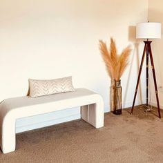 a white bench sitting next to a lamp on top of a carpeted room floor