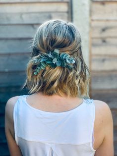 a woman with blonde hair wearing a white tank top and green leaves in her hair